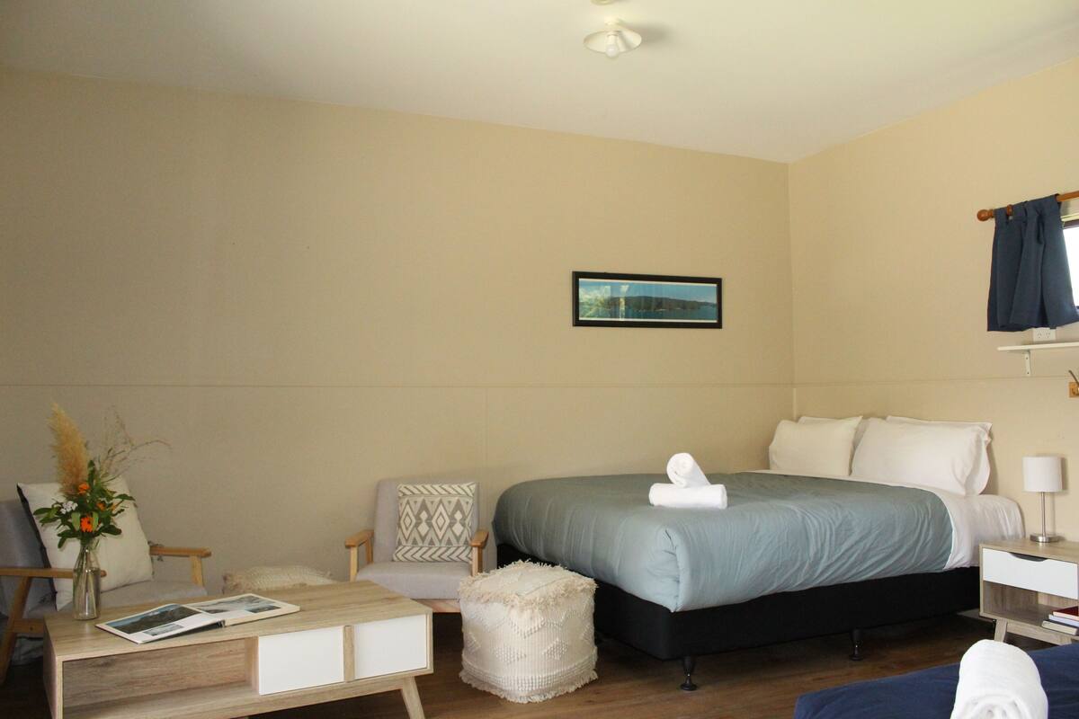 A hotel room with a bed, a chair, a small table, and a nightstand.