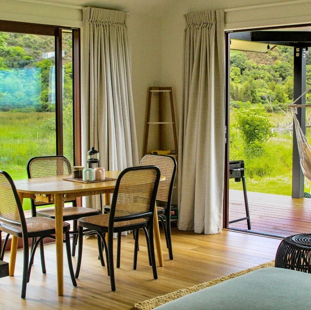 A dining area with a wooden table and chairs, a ladder, and a hammock outside.
