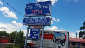 A Snowy River Inn sign with amenities like HBO, fax, phone, internet, low communication rates, AARP, coffee, and a microwave. There's a vacancy sign and a Haul truck nearby.