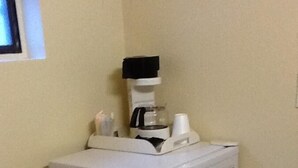 A compact refrigerator on a small shelf in a corner of a room with a tiled floor.