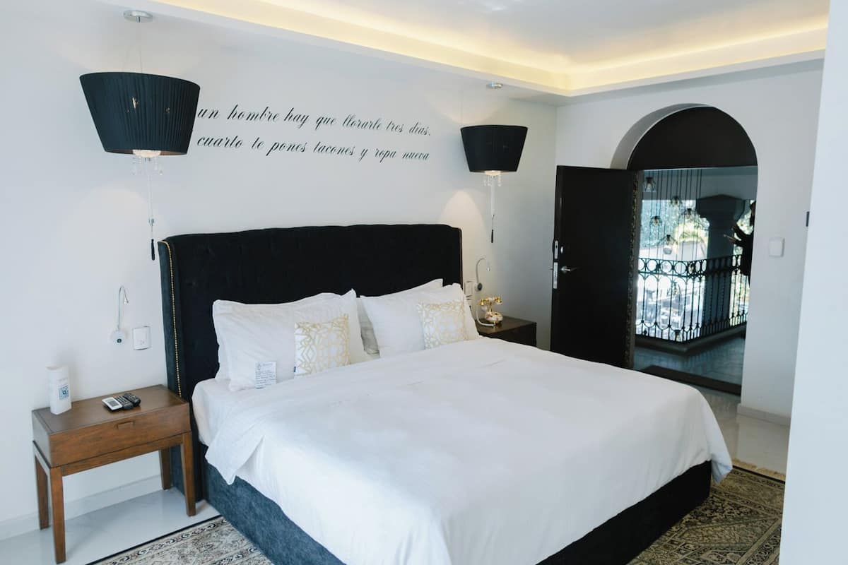 A modern bedroom with a large bed, a nightstand, a wall-mounted lamp, and a patterned rug.