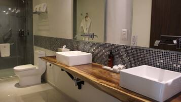 A modern bathroom with a wooden vanity, two sinks, a glass shower enclosure, and a mirror reflecting a robe and towel rack.