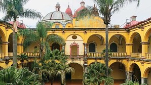 A courtyard with yellow buildings, arches, and palm trees.