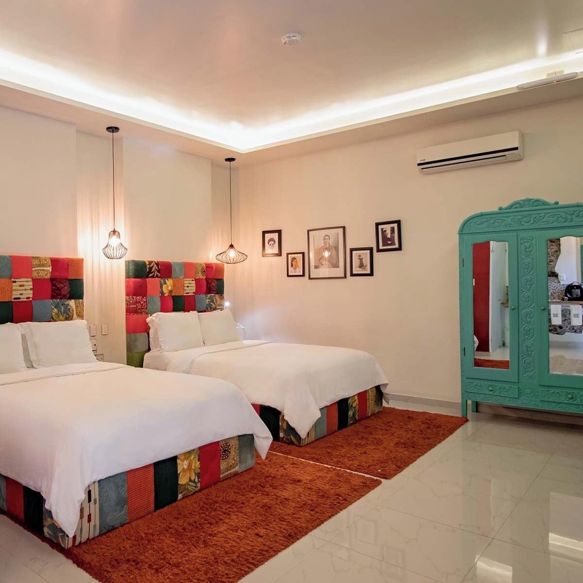 A hotel room with two beds, a red carpet, a green cabinet, and framed pictures on the wall.
