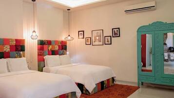 A hotel room with two beds, a red carpet, a green cabinet, and framed pictures on the wall.