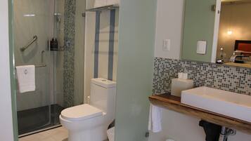 Un baño moderno con ducha de vidrio, inodoro blanco y tocador de madera con lavamanos.
