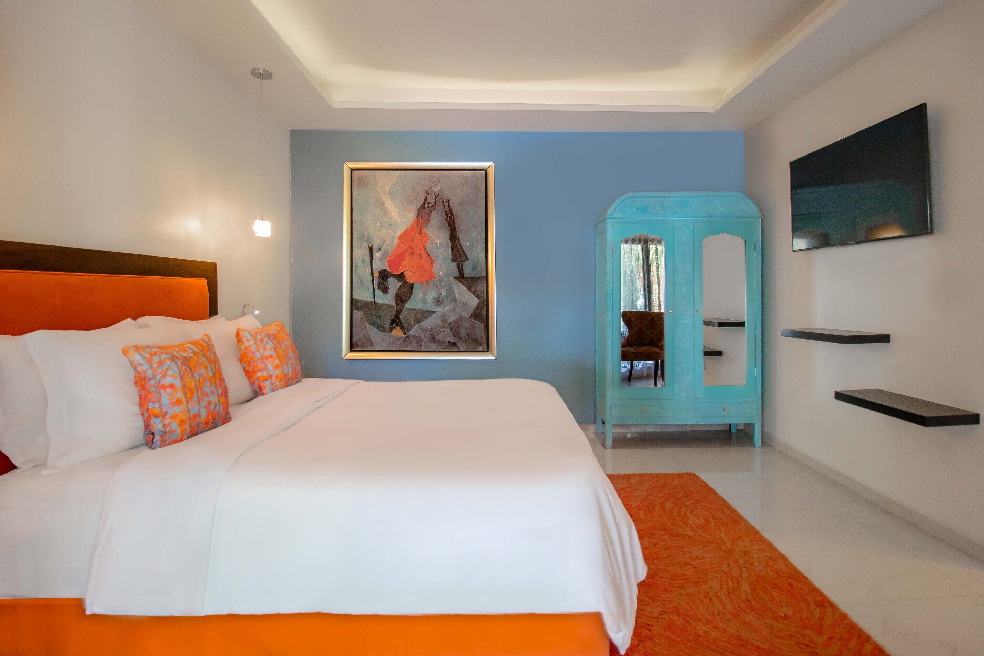 Una habitación de hotel moderna con una cama grande, un aparador azul y un cuadro en la pared.