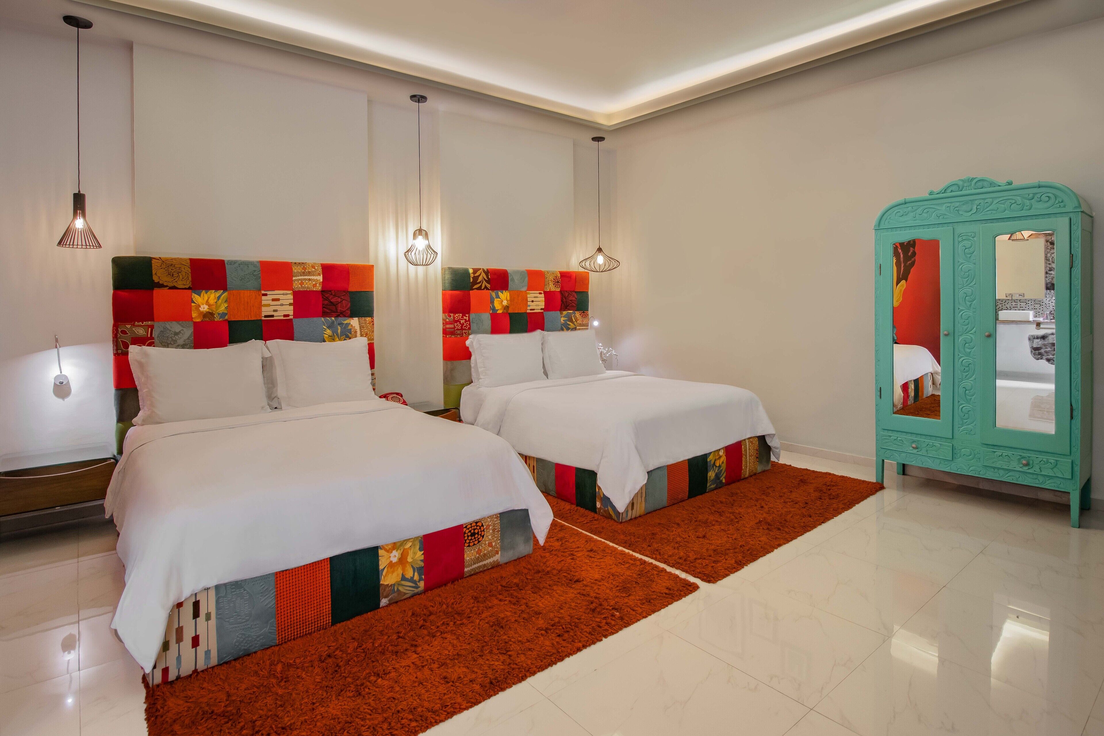 Une chambre d’hôtel avec deux lits, une armoire de couleur turquoise et une tête de lit colorée.
