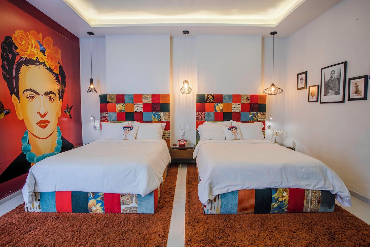 A hotel room with two beds, a colorful headboard, a large mural, and a brown carpet.