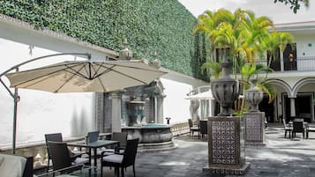 An outdoor patio area with tables and chairs, a fountain, and a decorative wall.