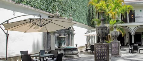 An outdoor patio area with tables and chairs, a fountain, and a decorative wall.