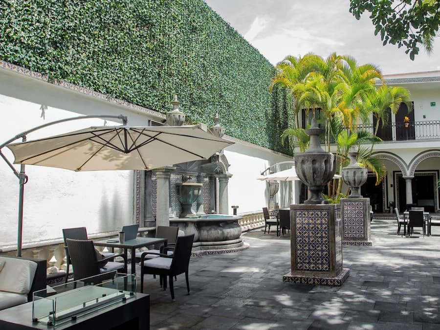Een terras buiten met tafels, stoelen, een fontein en een decoratieve muur.