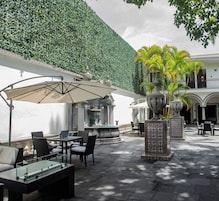 Un patio al aire libre con mesas y sillas, una fuente y un muro decorativo.