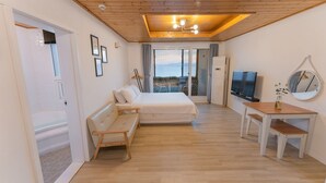 A bedroom with a bed, a desk, a TV, and a balcony with a view. - Bluegrad Pension (Namhae)