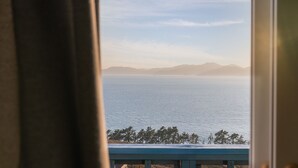 A view of a calm sea with mountains in the distance, seen through a window with a curtain. - Bluegrad Pension (Namhae)