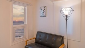 A room with a view of the sea at sunset, a black leather chair, a floor lamp, and a framed picture on the wall. - Bluegrad Pension (Namhae)