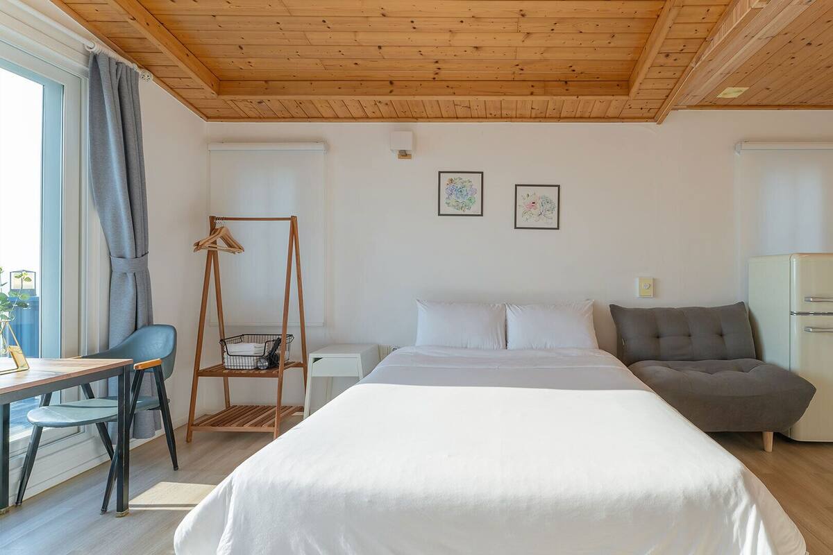 A bedroom with a bed, a desk, a chair, a sofa, and a wardrobe.