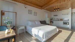 A bedroom with a bed, bedside table, and a small desk with a plant. There is a kitchenette with a microwave and a toaster. The room has wooden flooring and a wooden ceiling. - Bluegrad Pension (Namhae)