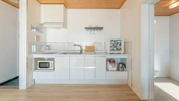 Cocina compacta con armarios blancos, un microondas, una tetera y un escurreplatos.