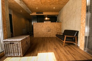 Una habitación con piso de madera, una silla de cuero negro, un cofre de mimbre y un mostrador de recepción con un logotipo.