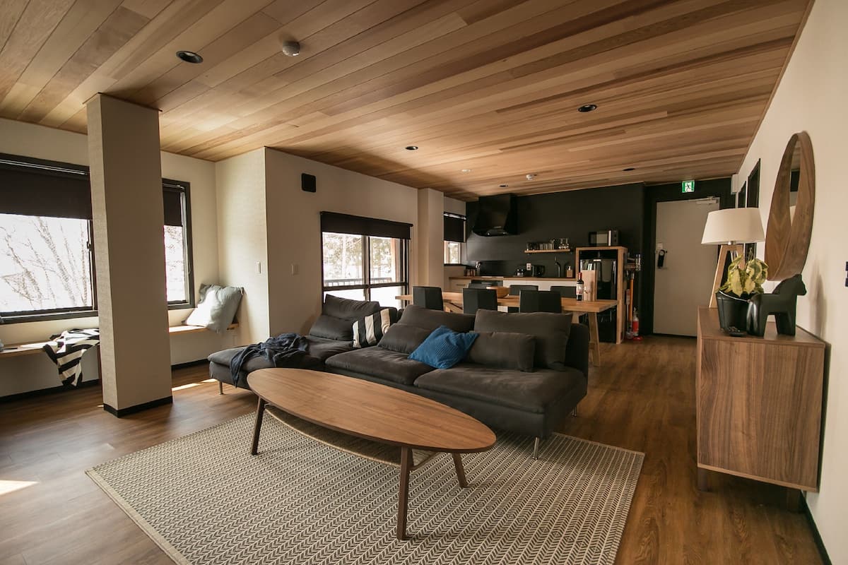 Una sala de estar moderna con techo de madera, un sofá de cuero oscuro, una mesa de centro de madera y una alfombra estampada.