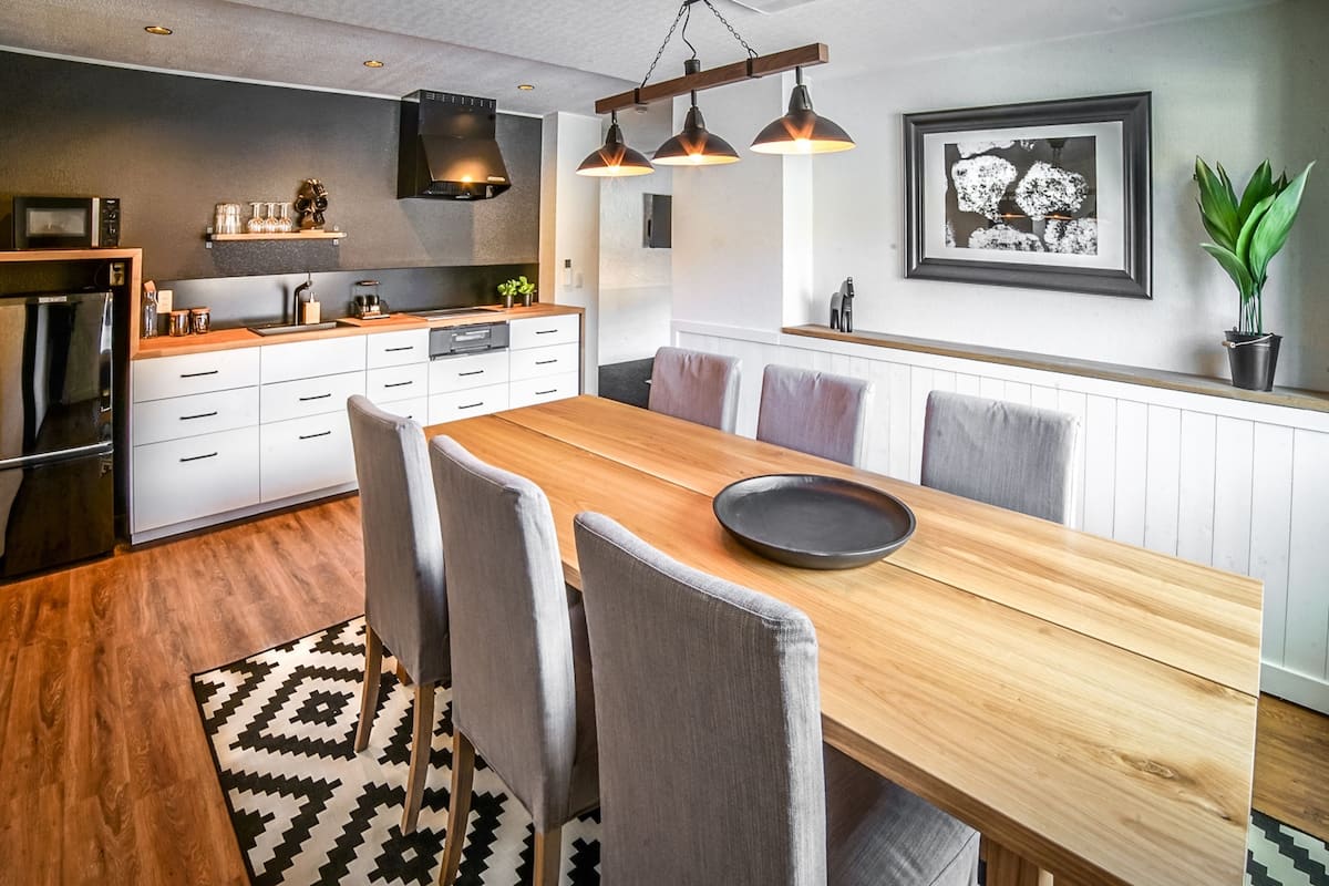 Una cocina moderna con una mesa y sillas de madera, horno empotrado e iluminación colgante.