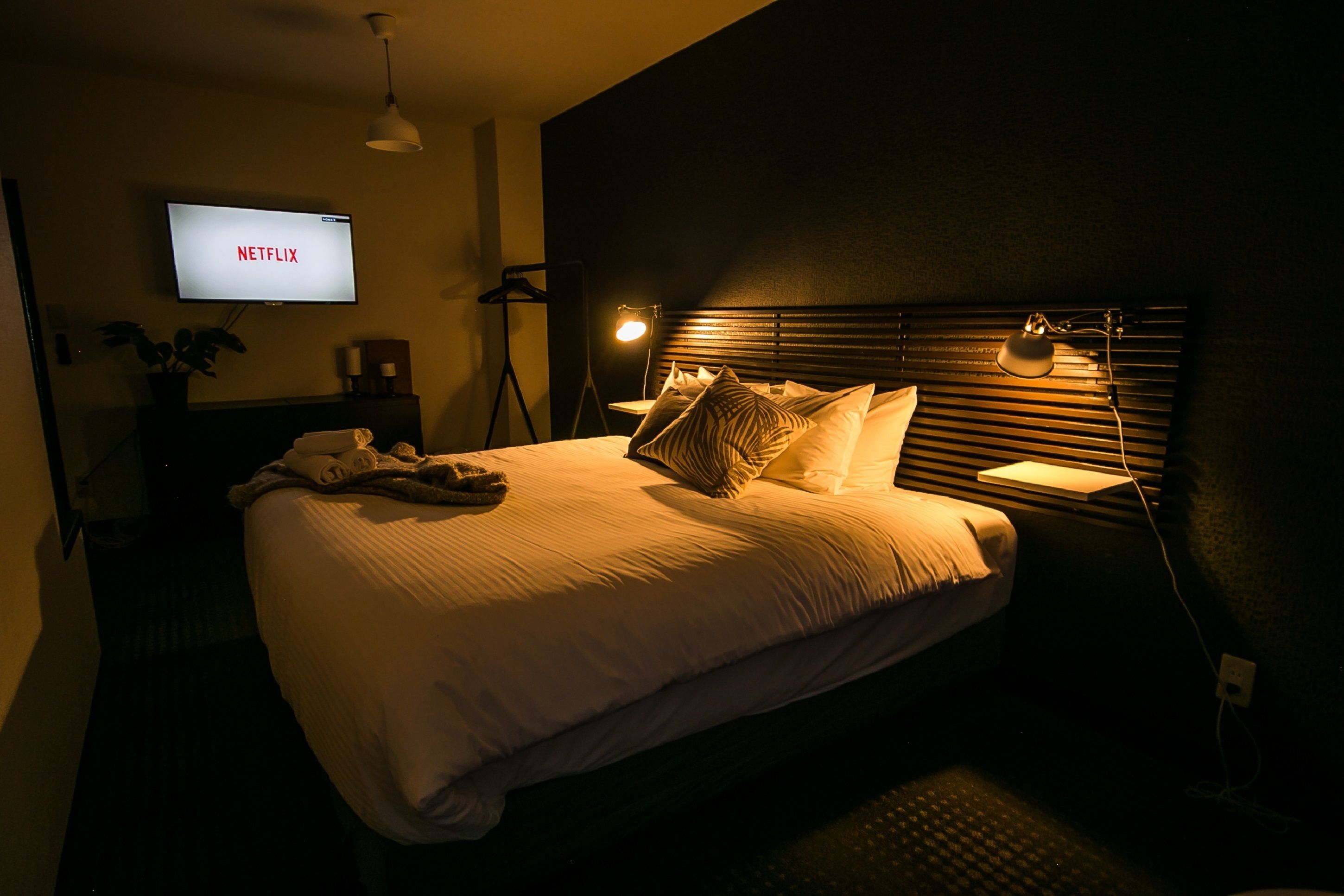 A hotel room with a bed, a TV displaying 'NETFLIX', a bedside lamp, and a nightstand.