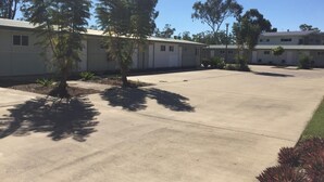 A building with a flat roof, multiple windows, and a paved parking area. - Swag Motel (Middlemount)