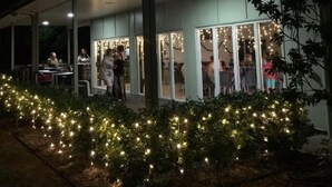 An outdoor covered area with tables and chairs, surrounded by greenery and string lights. - Swag Motel (Middlemount)