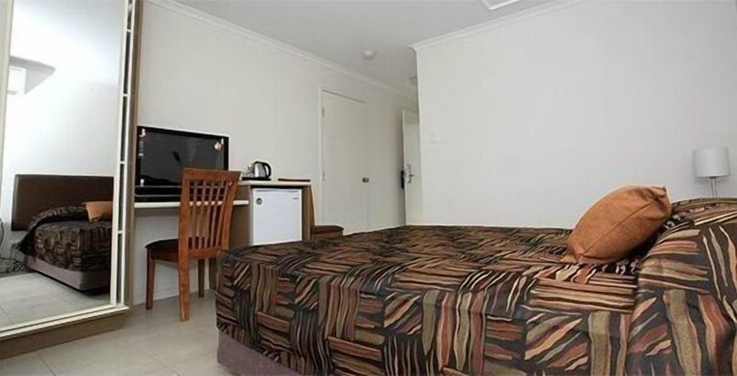 Een hotelkamer met een bed, een bureau met een televisie, een stoel en een kleine koelkast.