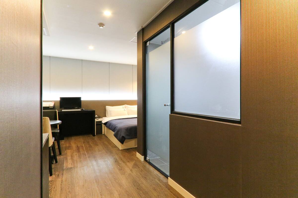 A modern hotel room with a bed, a desk with a chair, a television, and a sliding glass door.
