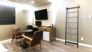 Une chambre de taille modeste équipée d’un bureau, d’un téléviseur à écran plat, d’un réfrigérateur et d’une chaise.