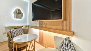 A modern living room with a round table, two sofas, a mounted TV, and a unique wall-mounted mirror. - Grandis Hotel (Busan)