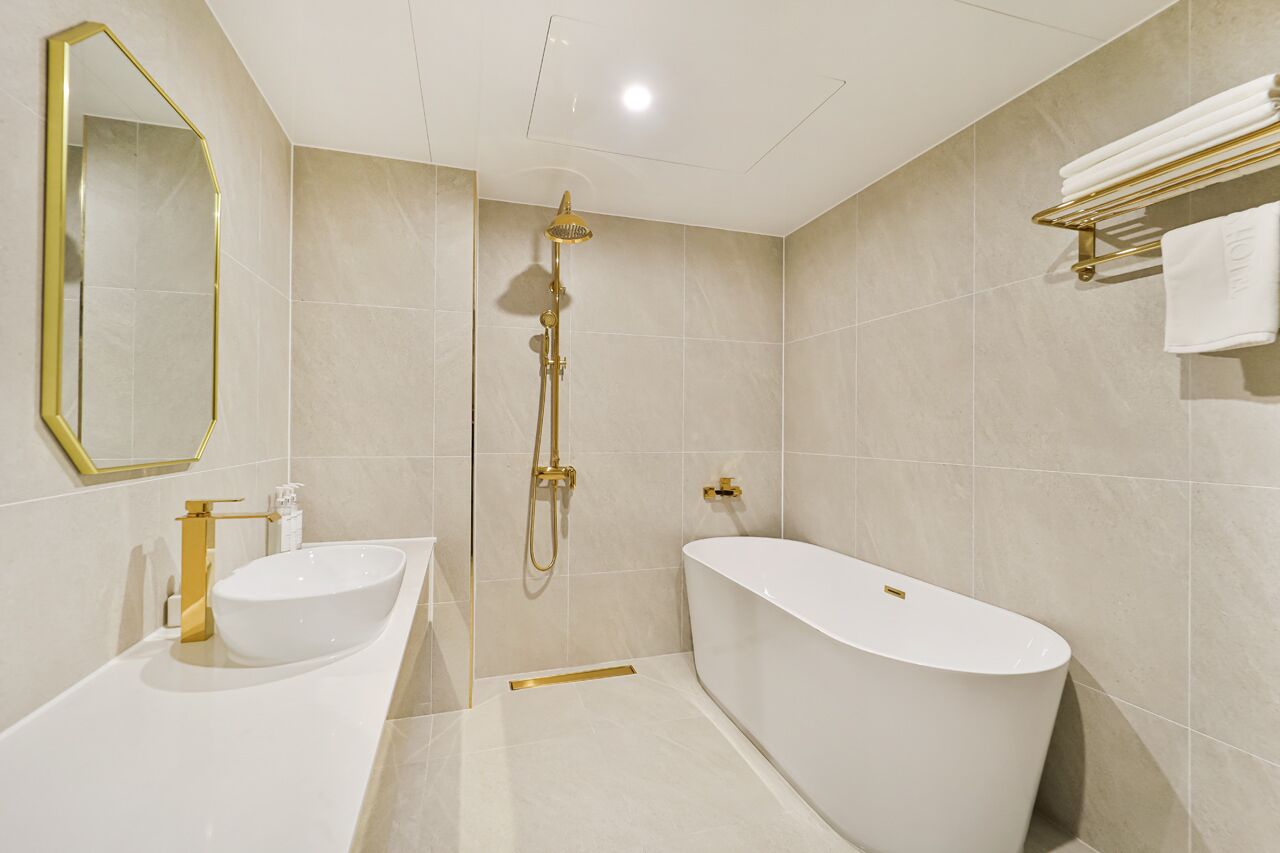 A modern bathroom with a freestanding bathtub, a vanity with a gold faucet, and a gold showerhead.