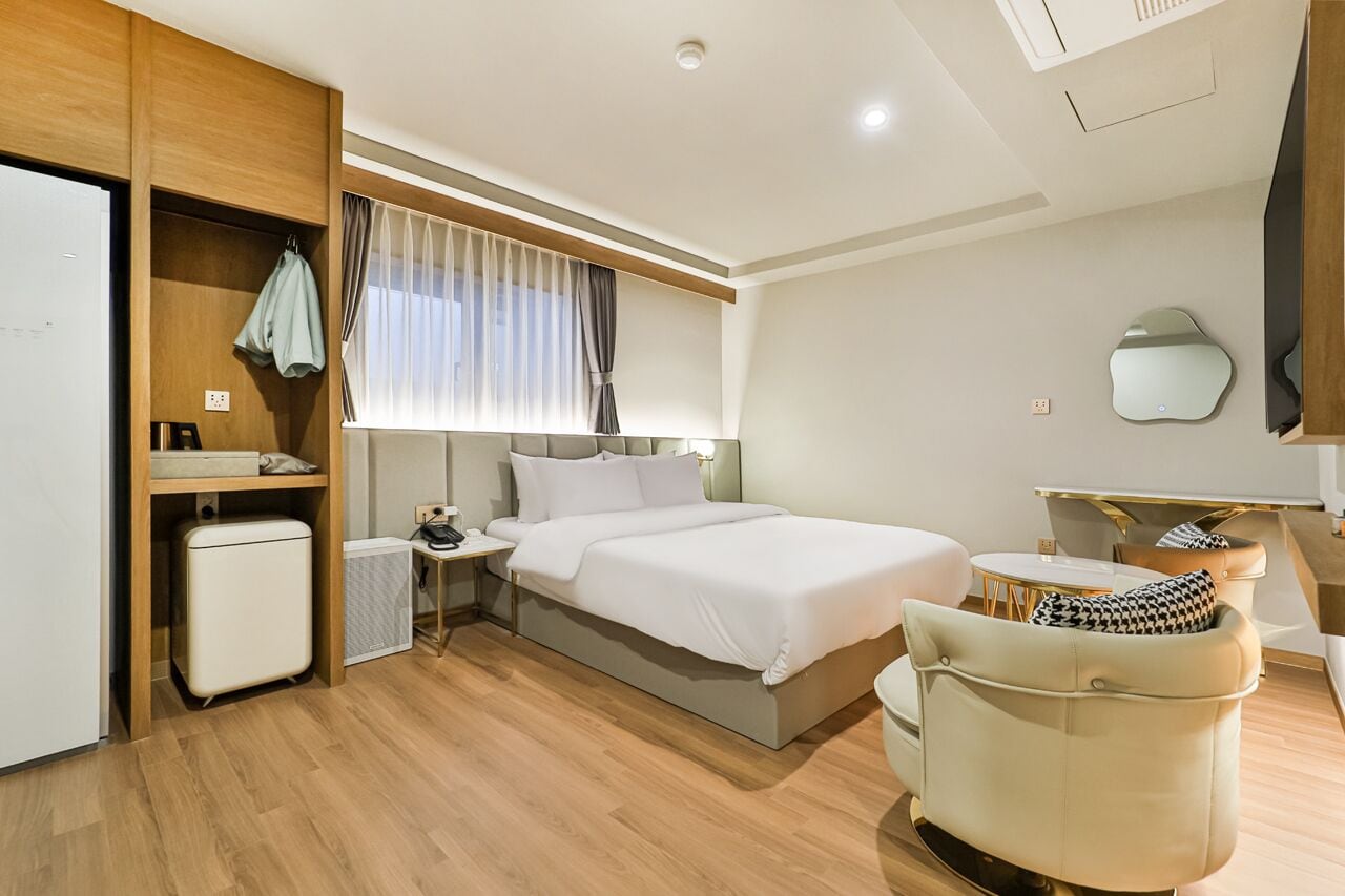 Une chambre d’hôtel moderne équipée d’un lit, d’une table de chevet, d’une chaise et d’un petit bureau avec un miroir.