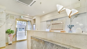 A hotel reception area with a marble counter, a sign for rates, and a plant. - Grandis Hotel (Busan)