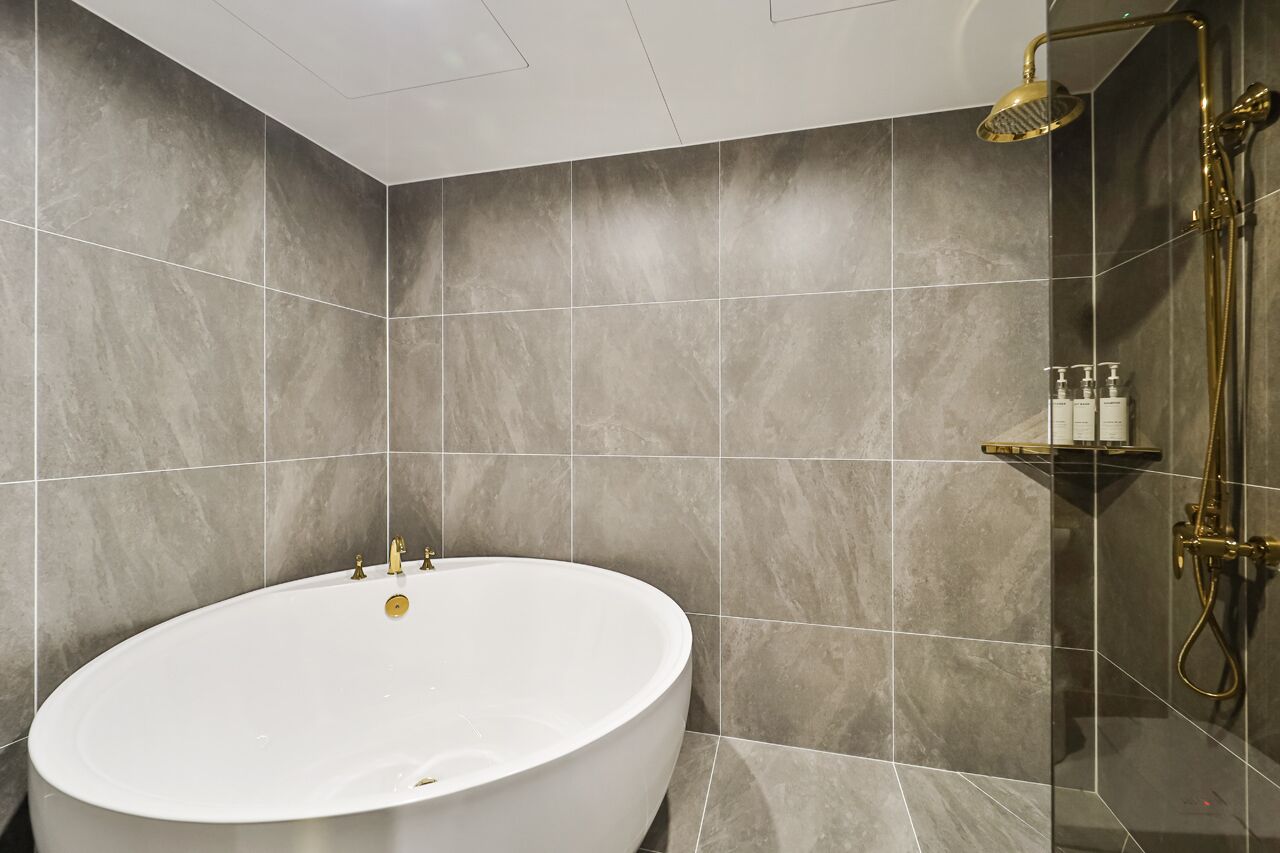 Un baño moderno con una bañera independiente, zona de ducha con mampara de vidrio y estante con artículos de aseo.