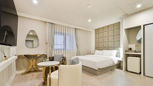 A hotel room with a bed, bedside tables, a TV, a seating area with a table and chairs, and a wardrobe. - Grandis Hotel (Busan)