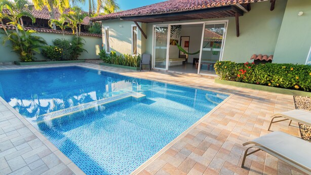 A swimming pool with tiled edges, adjacent lounge chairs, and a covered patio area. - Hotel PaloVerde Villas Campestres (Villavicencio)