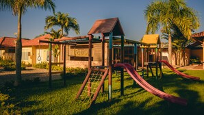 A playground with slides and climbing structures, surrounded by palm trees and buildings with red roofs. - Hotel PaloVerde Villas Campestres (Villavicencio)
