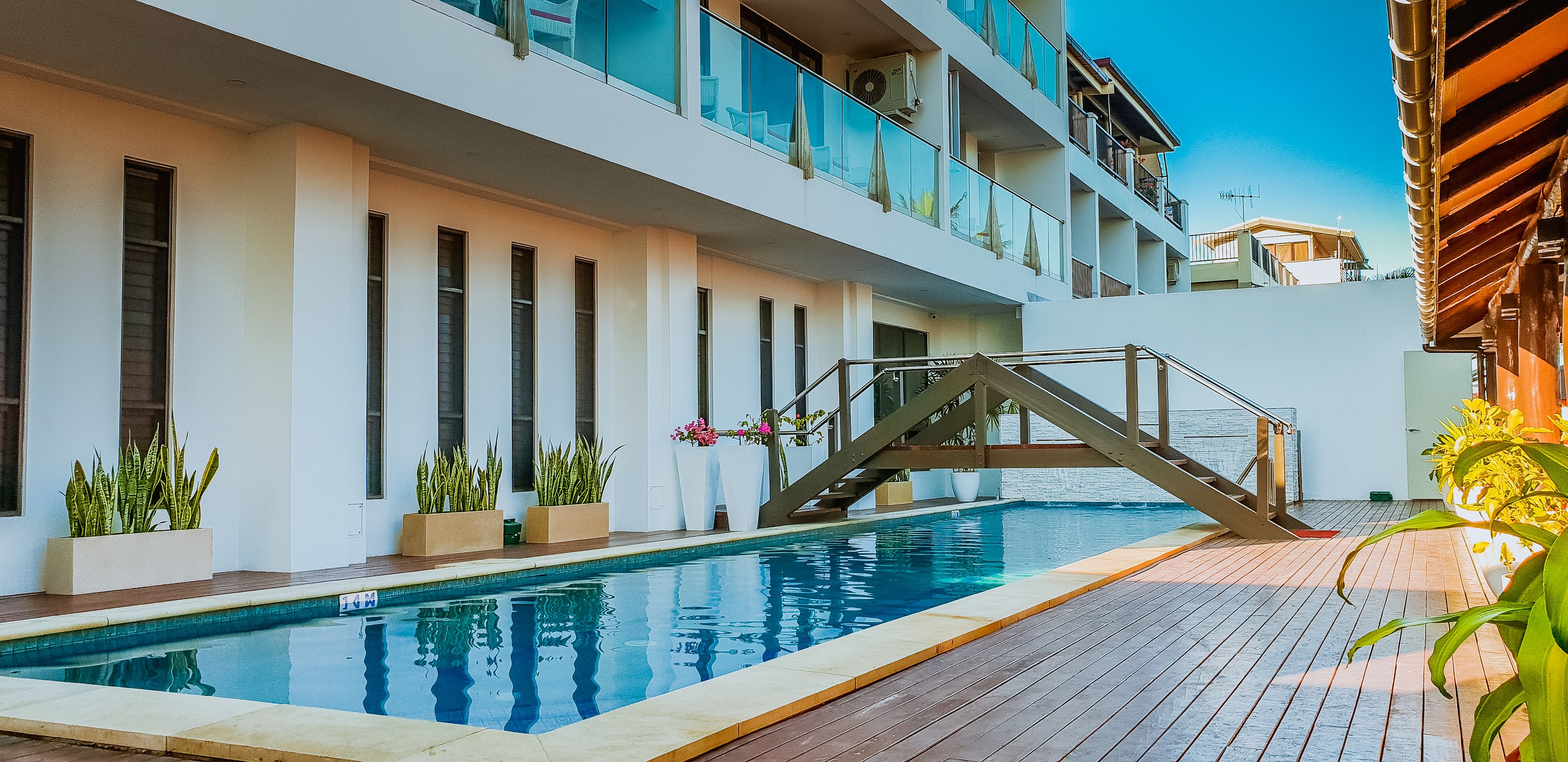 A modern hotel with a pool, outdoor seating, and a staircase leading to a balcony.