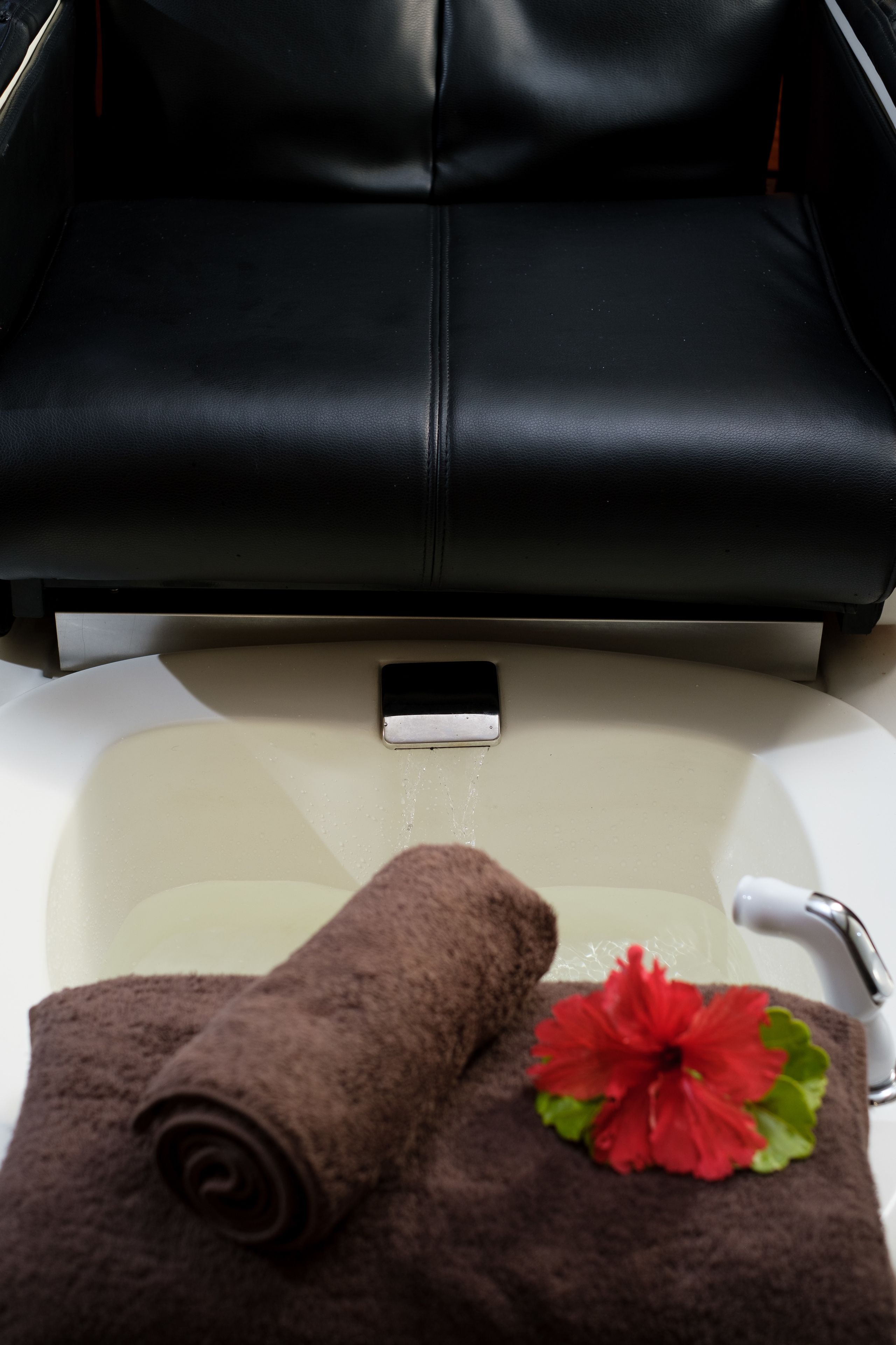 A black leather sofa, a smartphone, a brown towel, and a red hibiscus flower on a white sink.