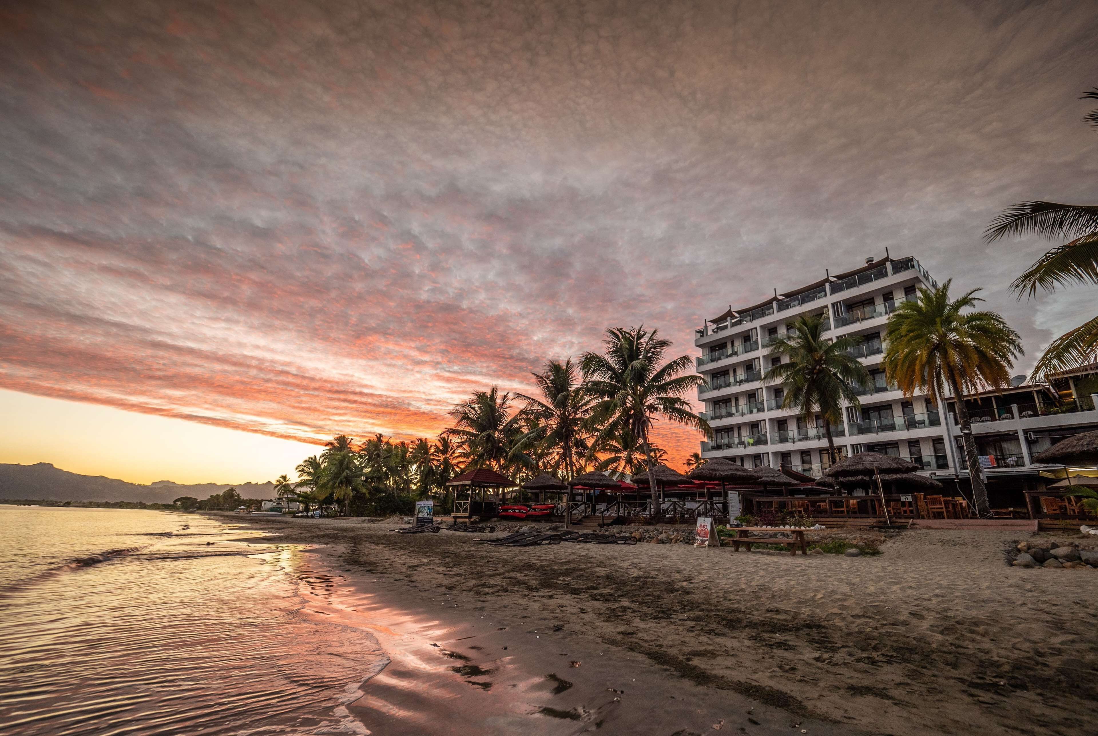 A beachfront hotel with multiple floors, palm trees, and beachside amenities.