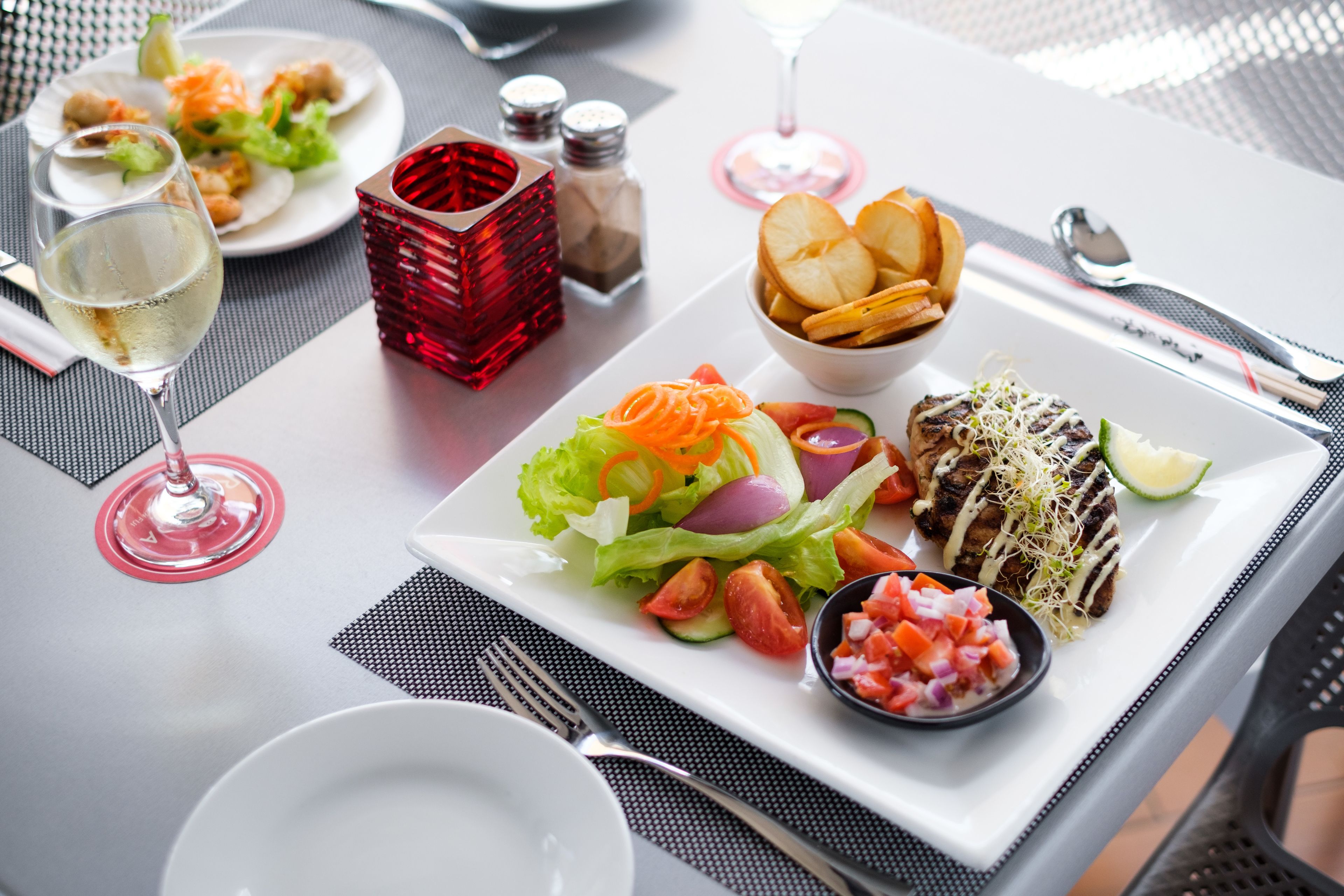 A table set with a plate of food, a glass of white wine, and condiments.