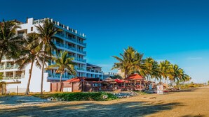 Ein Hotel direkt am Strand mit mehreren Etagen, Palmen und Annehmlichkeiten am Strand.