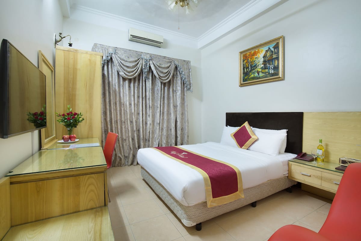 A hotel room with a bed, a desk, a chair, a nightstand, a mirror, and a painting on the wall.