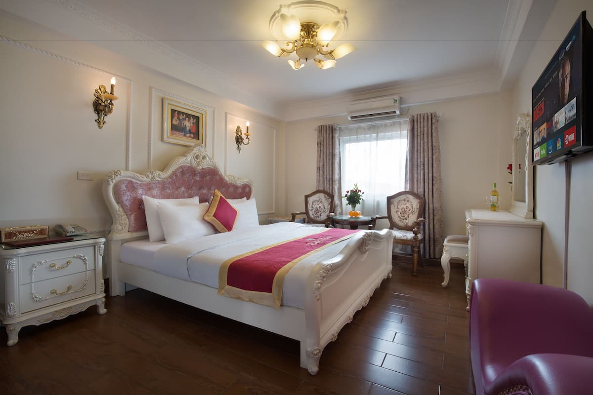 A well-appointed bedroom with a large bed, a vanity, a television, and a chandelier.