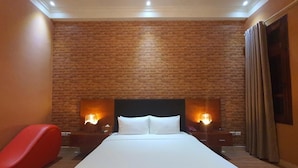 A hotel room with a large bed, brick wall, two bedside lamps, a red chair, and a window with curtains. - Ruby Hotel (Hanoi)