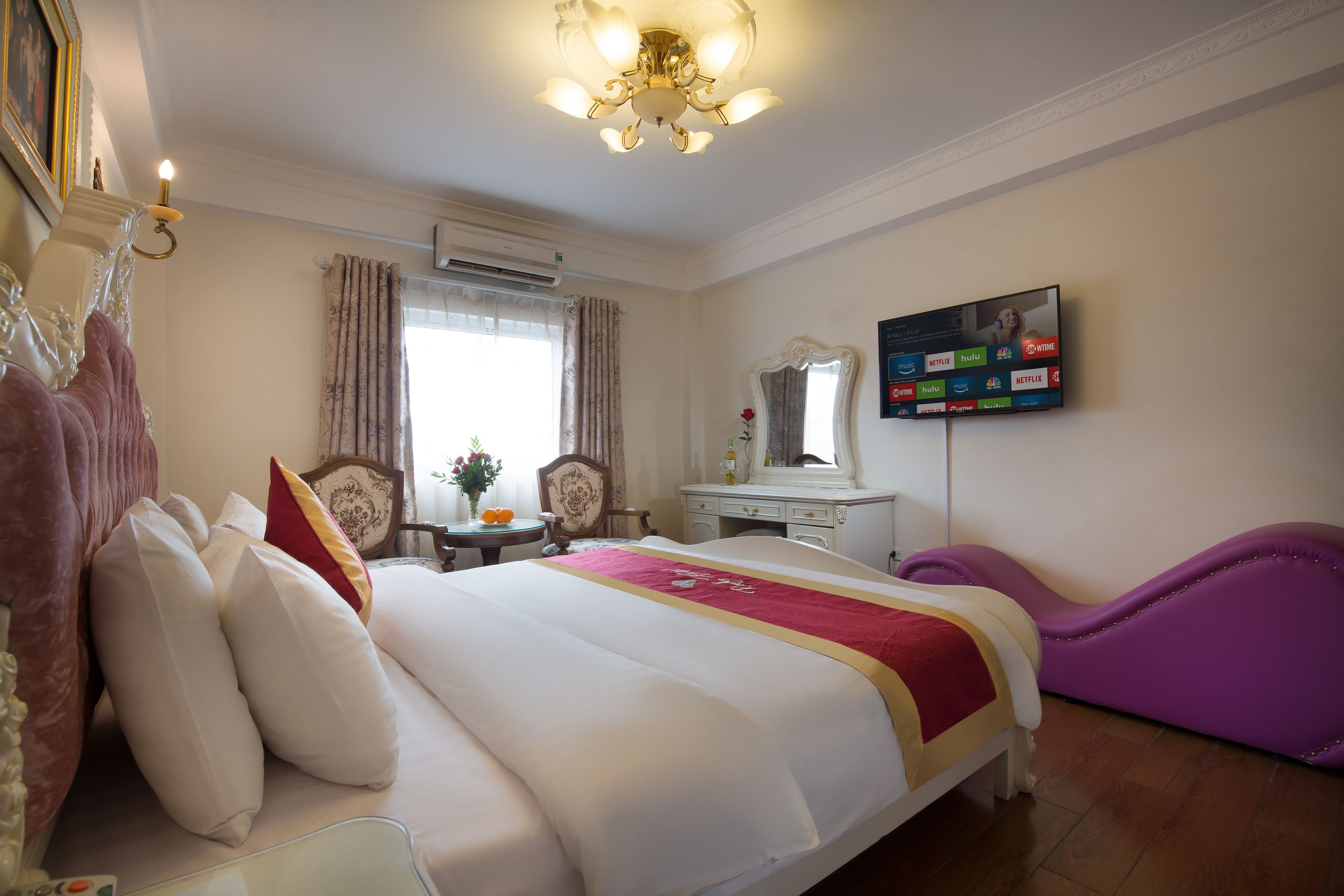 A hotel room with a large bed, a vanity with a mirror, a television on the wall, and a window with curtains.