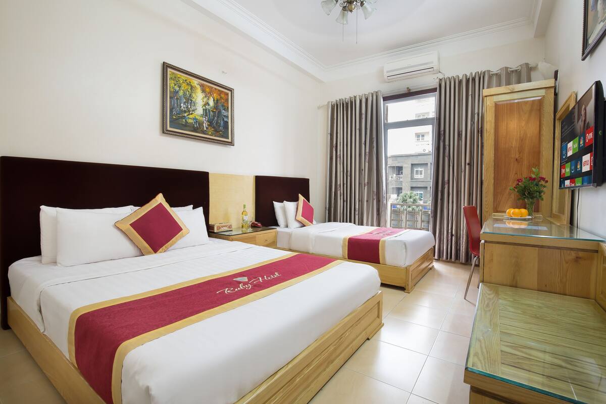 A hotel room with two beds, a wooden desk, a mirror, and a painting on the wall.